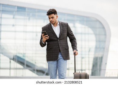 Young Arabian Man Standing Outside In Front Of Airport Gate And Checking His Flight Schedule On Phone. Young Man Browsing On Cellphone, Typing Message. Urban, Travel And Communication Concept