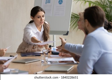 Young Arabic businesswoman share handout materials to diverse colleagues at meeting in office. Millennial female employee pass give paperwork document to coworker at business briefing. - Shutterstock ID 1840228651