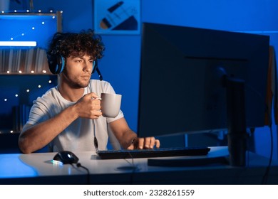 Young arabic gamer wearing headphones playing video game on personal computer, play in eSport cyber games tournament in neon light, drinking coffee at night. Copy space - Powered by Shutterstock