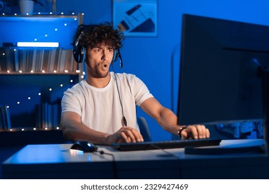 Young arabic gamer wearing headphones playing video game on personal computer, play in eSport cyber games tournament in neon light. Funny teenager is excited because of seen virtual video. Copy space - Powered by Shutterstock