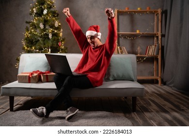 Young arabic man in red christmas santa hat very happy and rejoices sitting in front of laptop. Christmas sales, Boxing Day concept. Copy space - Powered by Shutterstock