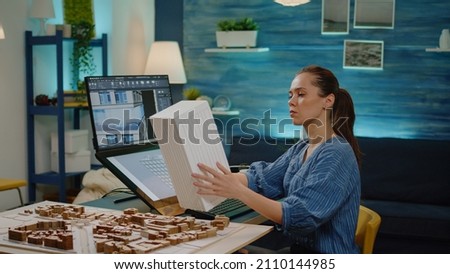 Young architect holding maquette model in hand working on building layout for construction development. Engineer woman with blueprint plan analyzing touch screen monitor in office. [[stock_photo]] © 