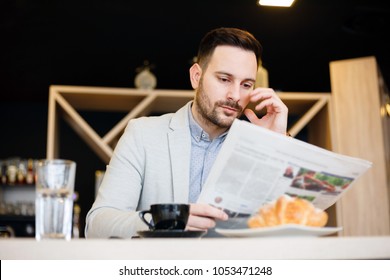 Young architect reading newspapers while having a breakfast in a modern cafe.