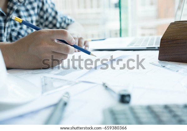 young\
architect working on real estate project at workplace. Male\
engineer hand working with living house blueprint at office.\
Business, people, construction and building\
concept