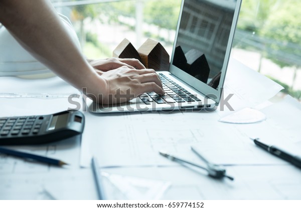 young architect working on real estate project at
workplace. Male engineer hand working with laptop computer and
living house blueprint at office. Business, people, construction
and building concept
