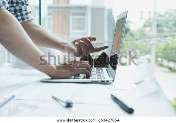 young architect working on real estate project at
workplace. Male engineer hand working with laptop computer and
living house blueprint at office. Business, people, construction
and building concept