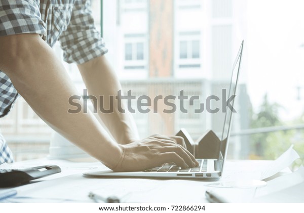 young architect working on real estate project at\
workplace. Male engineer hand working with laptop computer and\
living house blueprint at office. Business, people, construction\
and building concept
