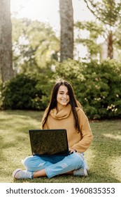 A young Argentinian female student in a yellow sweater sitting on the grass with a laptop on her legs