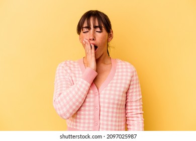 Young Argentinian woman isolated on yellow background yawning showing a tired gesture covering mouth with hand.