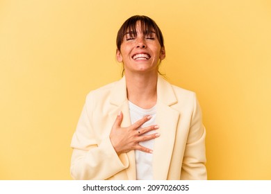 Young Argentinian woman isolated on yellow background laughs out loudly keeping hand on chest.