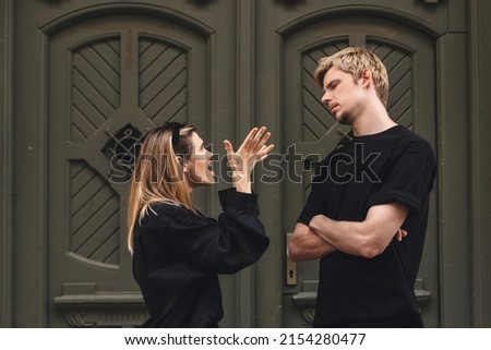 Young arguing sad couple two friends family man woman in casual clothes screaming scolding together walking outdoor near door of home. Woman yelling at man. Couple arguing, having relationship problem
