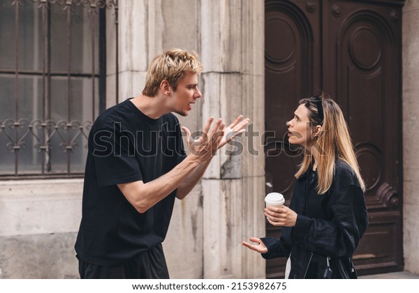 Young arguing sad couple two friends family man\
woman in casual clothes screaming scolding together walking outdoor\
near door of home. Man yelling at woman. Couple arguing, having\
relationship problem