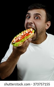 Young Armenian Man Eating A Messy Hotdog Isolated On Black Background