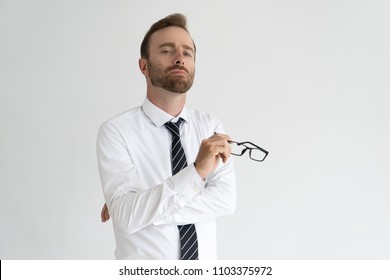 Young arrogant business expert posing for camera. Vain serious Caucasian man with pained face expression holding glasses. Self importance and ego concept