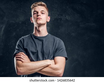 Young Arrogant Male Is Looking To The Camera Crossed His Hands Over Dark Background.