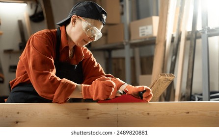 Young Artisan woman Using Hand Plane to Shape a Wood plank. Female carpenter working in a woodworking workshop. Copy space - Powered by Shutterstock