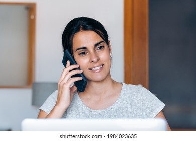 Young Artisan Woman Working From Home And Talking On The Phone. She Is Sitting In Her Desk.