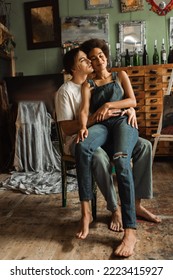 Young Artist Hugging Sensual African American Woman In Denim Overalls Sitting On His Laps With Closed Eyes