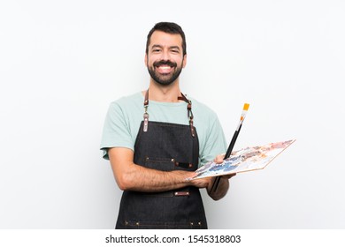 Young artist man holding a palette over isolated background keeping the arms crossed in frontal position