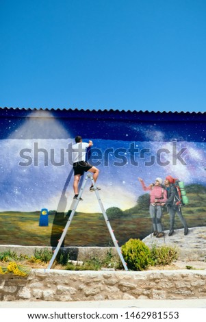 Young artist painting a graffiti about peace and pilgrimage along the St. James Way to Santiago de Compostela, Spain