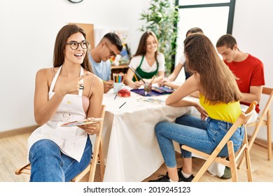 Young artist woman drawing at art studio pointing thumb up to the side smiling happy with open mouth  - Powered by Shutterstock