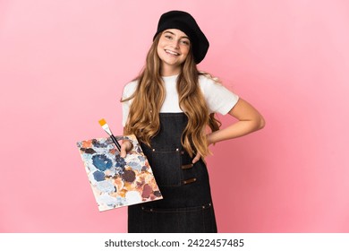 Young artist woman holding a palette isolated on pink background posing with arms at hip and smiling - Powered by Shutterstock