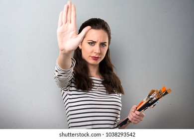 Young artist woman making stop sign on grey background