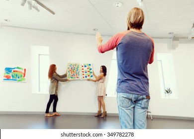 Young Artists In Gallery Hanging Together Painting On Walls