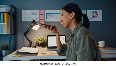 Young Asia Business Lady Freelance Using Smart Phone Voice Assistant App Or Loudspeaker Talking With Friends At Office Night. Work From House, Remotely, Social Distance, Quarantine For Coronavirus.