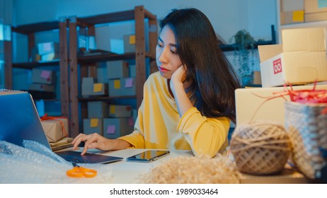 Young Asia Businesswoman Look Around Room Full Of Product Stuff And Parcel Box Feel Stress And Upset With Bad Sell In Home Office At Night. Small Business Owner, Online Market Delivery Concept.