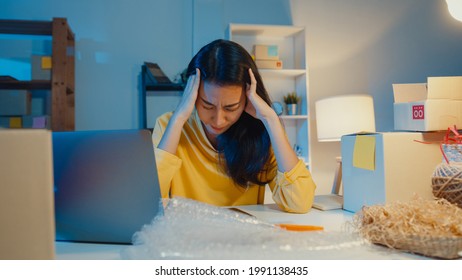 Young Asia Businesswoman Look Around Room Full Of Product Stuff And Parcel Box Feel Stress And Upset With Bad Sell In Home Office At Night. Small Business Owner, Online Market Delivery Concept.