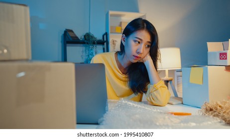 Young Asia Businesswoman Look Around Room Full Of Product Stuff And Parcel Box Feel Stress And Upset With Bad Sell In Home Office At Night. Small Business Owner, Online Market Delivery Concept.