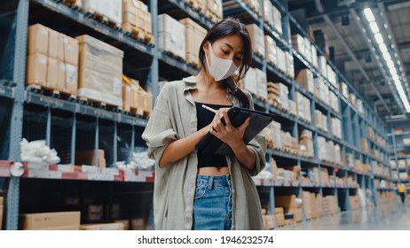 Young Asia businesswoman manager wear face mask looking for goods using digital tablet checking inventory levels stand in retail shopping center. Distribution, Logistics, Packages ready for shipment. - Powered by Shutterstock