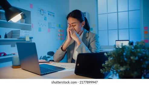 Young Asia businesswoman sit with laptop and tablet on desk rubbing eye feel pain and tired from overwork in office at night. Female suffer of office syndrome long work, Mental Health workplace. - Shutterstock ID 2177899947