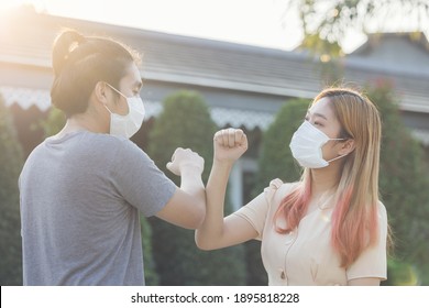 Young Asia Couple Wearing Face Mask Outdoors Say Hello With Elbows Outdoors. No Hugs, No Kisses, No Shake Hands. Friends Shaking Elbows Outdoors