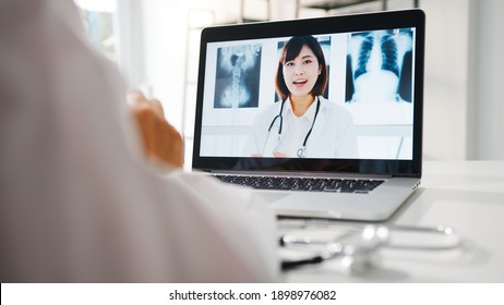 Young Asia female doctor in white medical uniform using laptop talking video conference call with senior doctor at desk in health clinic or hospital. Social distancing, quarantine for corona virus. - Powered by Shutterstock