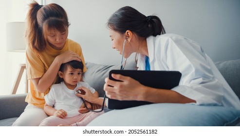 Young Asia female pediatrician hold stethoscope exam little girl patient visit doctor with mother sit on couch in living room at house. Medical care insurance, Visit patient at home concept.