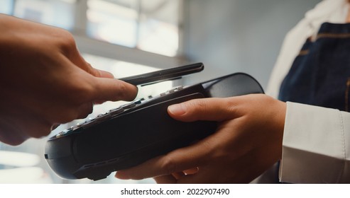 Young Asia Female Self Service Use Mobile Phone Pay Contactless With Credit Card Reader Machine At Cafe Restaurant. Owner Small Business, Cashless Technology And Money Transfer Concept. Close Up Shot.