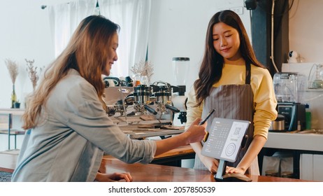 Young Asia female self service use mobile phone pay contactless with tablet at cafe restaurant. Girl barista talking receive orders from customer at bar counter in coffee shop. Owner small business. - Powered by Shutterstock