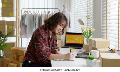 Young asia freelance seller woman happy typing check on laptop computer busy at home office desk use digital tablet in fashion studio SME online store social e-commerce sale page service web support.