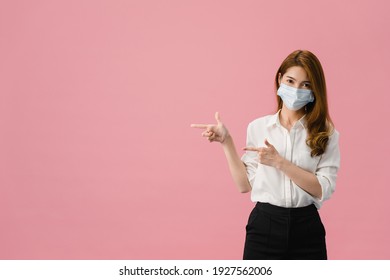 Young Asia Girl Wear Medical Face Mask Shows Something At Blank Space With Dressed In Casual Cloth And Look At Camera Isolated On Blue Background. Social Distancing, Quarantine For Corona Virus.