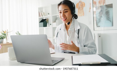 Young Asia Lady Arzt in weißer medizinischer Uniform mit Stethoskop mit Laptop-Gespräch-Videokonferenz mit Patient am Schreibtisch in der Gesundheitsklinik oder im Krankenhaus. Beratungs- und Therapiekonzept.