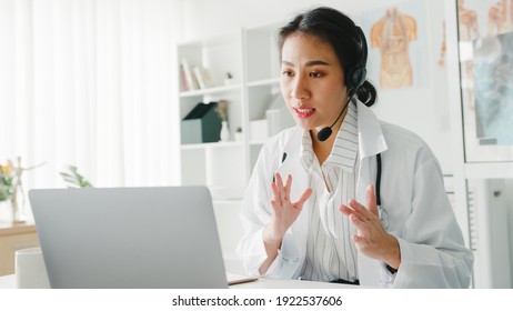 Young Asia lady doctor in white medical uniform with stethoscope using computer laptop talking video conference call with patient at desk in health clinic or hospital. Consulting and therapy concept.