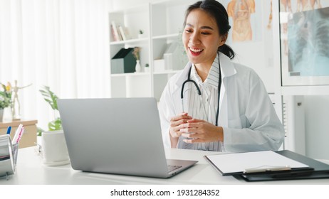 Young Asia Lady Arzt in weißer medizinischer Uniform mit Stethoskop mit Laptop-Gespräch-Videokonferenz mit Patient am Schreibtisch in der Gesundheitsklinik oder im Krankenhaus. Beratungs- und Therapiekonzept.