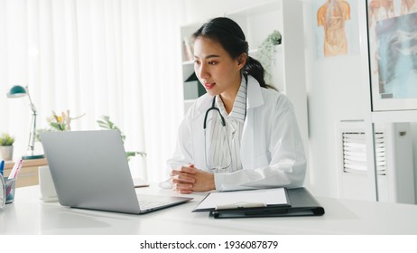 Young Asia lady doctor in white medical uniform with stethoscope using computer laptop talking video conference call with patient at desk in health clinic or hospital. Consulting and therapy concept.
