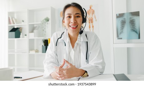 Young Asia lady doctor in white medical uniform with stethoscope using computer laptop talk video conference call with patient, looking at camera in health hospital. Consulting and therapy concept.