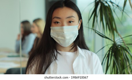 Young Asia Lady In Medical Mask Standing In Contemporary Meeting Room. Portrait Of Successful Beautiful Executive Asian Businesswoman Smart Casual Wear Looking At Camera In Modern Office Workplace