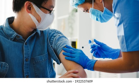 Young Asia Lady Nurse Giving Covid-19 Or Flu Antivirus Vaccine Shot To Senior Male Patient Wear Face Mask Protection From Virus Disease At Health Clinic Or Hospital Office. Vaccination Concept.