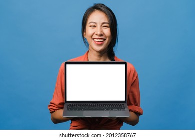 Young Asia Lady Show Empty Laptop Screen With Positive Expression, Smiles Broadly, Dressed In Casual Clothing Feeling Happiness Isolated On Blue Background. Computer With White Screen In Female Hand.