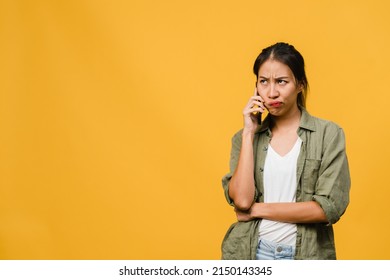 Young Asia Lady Talk By Phone With Negative Expression, Excited Screaming, Cry Emotional Angry In Casual Cloth And Stand Isolated On Yellow Background With Blank Copy Space. Facial Expression Concept.